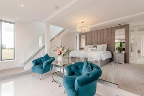 A modern bedroom with a large bed, a glass desk, two blue armchairs, a chandelier, and a large mirror. - 1 Bed in Claxby St. Andrew (oc-r42838) (Claxby St. Andrew)