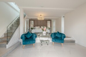 A modern living room with a glass coffee table, two teal armchairs, a chandelier, and a staircase leading to a bedroom. - 1 Bed in Claxby St. Andrew (oc-r42838) (Claxby St. Andrew)