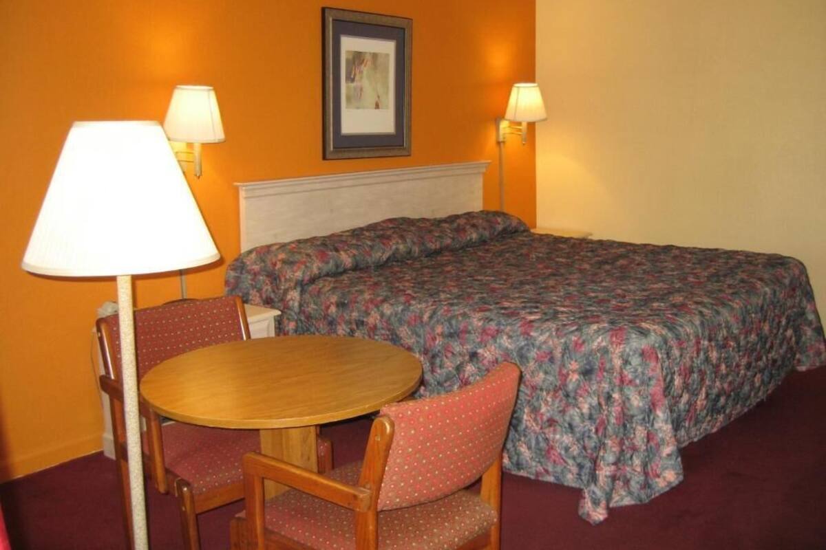 A hotel room with a bed, two lamps, a round table, and two chairs.