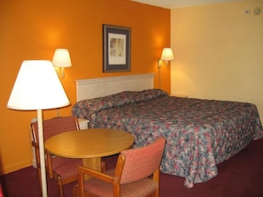 Una habitación de hotel con una cama, dos lámparas, una mesa redonda y dos sillas.