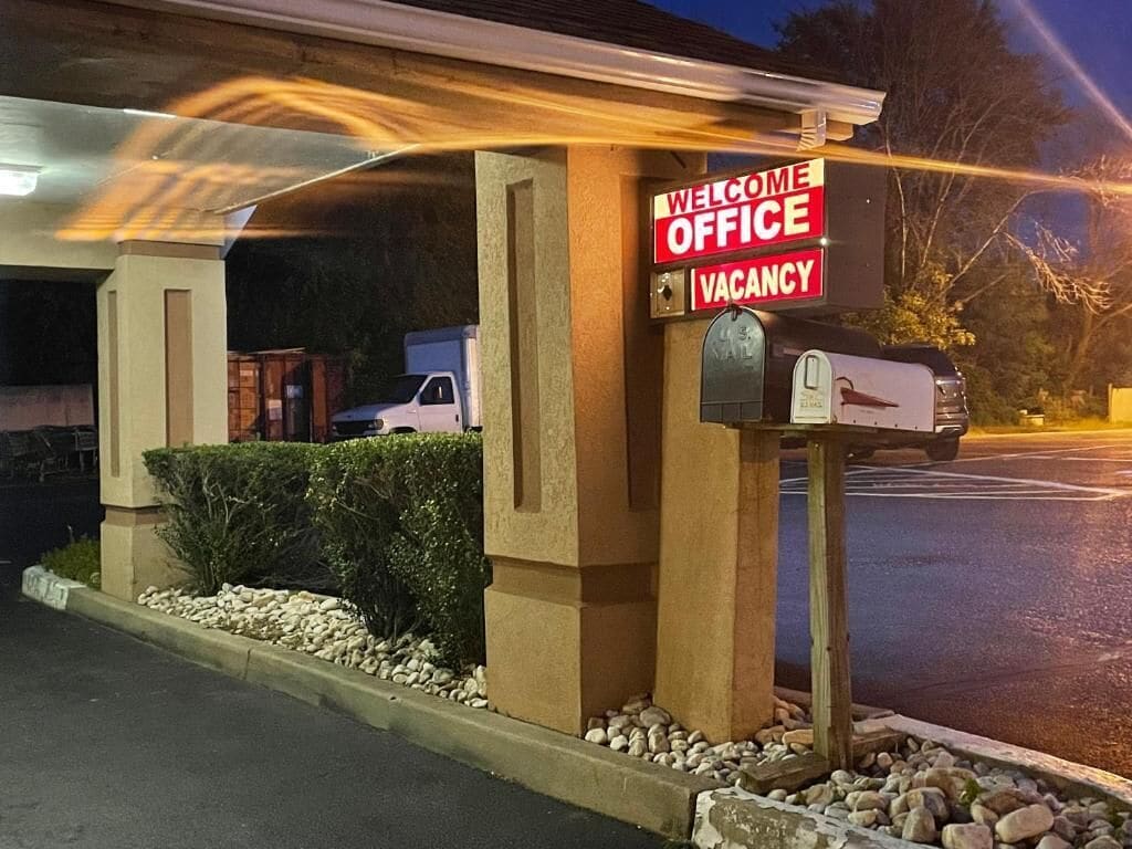 A building with a 'Welcome Office Vacancy' sign, a mailbox, and a parked vehicle.