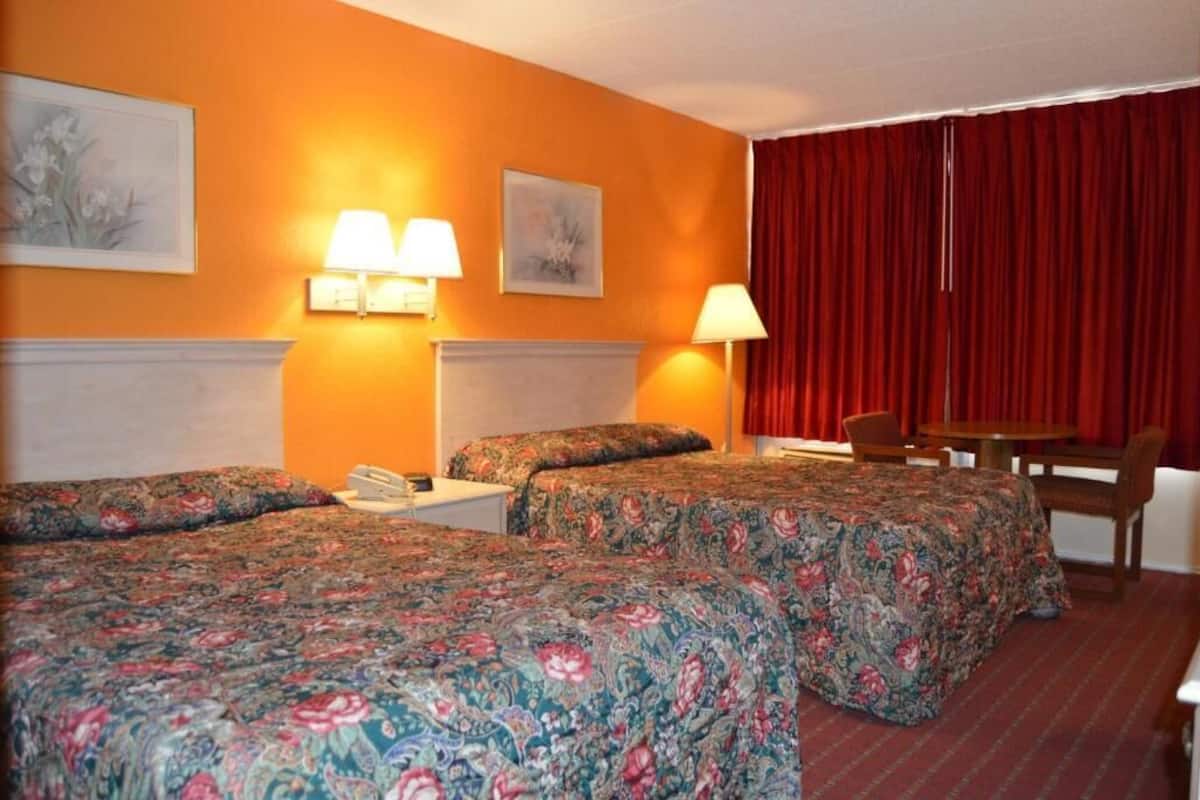 A hotel room with two beds, a red curtain, and a small table with chairs.