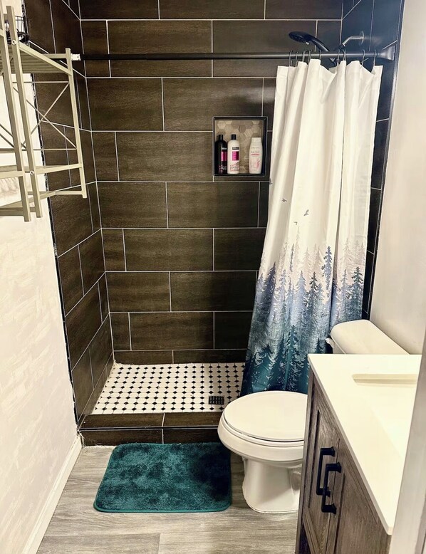 Un baño con ducha, inodoro y un estante con artículos de aseo.