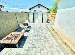 Laatoitettu patio, jossa on grilli, pieni pöytä ja kaksi tuolia.