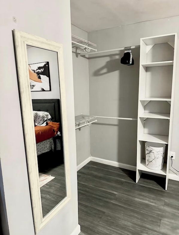 Ein begehbarer Kleiderschrank mit offenen Regalen, einem Spiegel und einem Bett mit roter Decke.