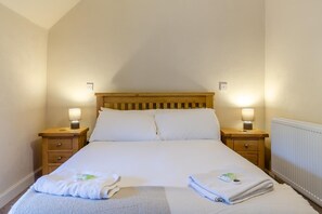 Una cama individual con cabecera de madera, dos mesitas de noche con lámparas y un radiador.