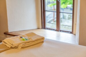 Una cama bien tendida con una toalla doblada y artículos de tocador, ubicada cerca de una ventana con vistas a zonas verdes.