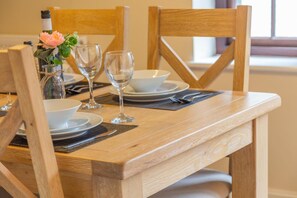 Una mesa de comedor de madera dispuesta con platos, vasos y una botella de vino, junto a un florero con flores.