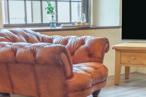 Un sofá de cuero marrón en una habitación con una mesita de madera y una ventana con persianas.
