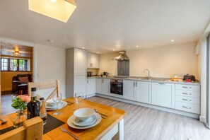 A modern kitchen with white cabinets, a built-in oven, and a dining area with a wooden table set for two. - 3 Bed in Lanreath (oc-j42768) (Lanreath)