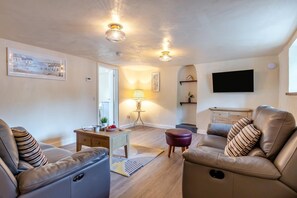 A living room with leather sofas, a coffee table, a lamp, a flat-screen TV, and a painting on the wall. - 3 Bed in Lanreath (oc-j42768) (Lanreath)