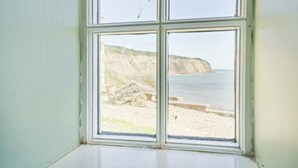 Une fenêtre donnant sur une plage, des falaises et une clôture.