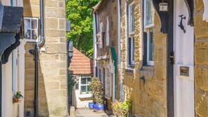 Une rue étroite bordée d’immeubles en pierre, avec un magasin bien visible et un petit espace aménagé en jardin.