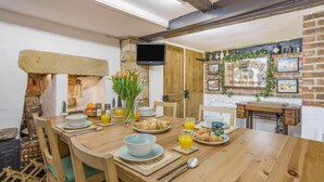 Une table à manger en bois, avec des aliments pour le petit-déjeuner, un mur en briques et un téléviseur fixé au mur.