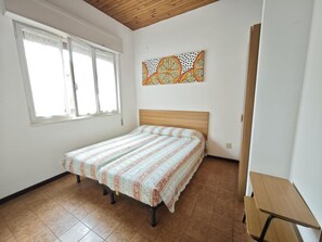 Ein Schlafzimmer mit einem Bett, einem Fenster, einer Holzbalkendecke und einem an der Wand hängenden Kunstwerk.