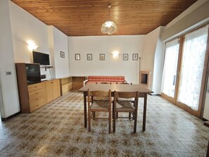 Ein Zimmer mit Holzboden, einem Esstisch mit Stühlen, einem Fernseher und gerahmten Bildern an der Wand.