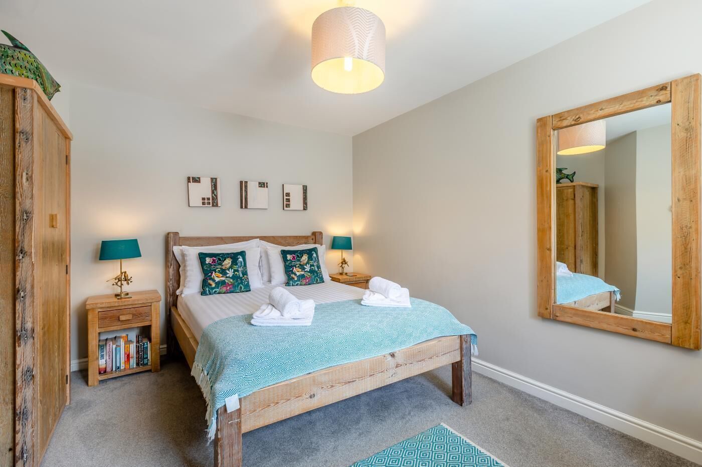 A bedroom with a wooden bed, a bedside table with a lamp, a mirror, and a bookshelf.