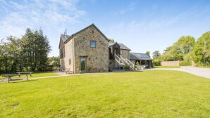 A stone building with a covered outdoor area, a grassy lawn, and a paved path. - 6 Bed in Llansantffraid (oc-r42827) (Llansantffraid)