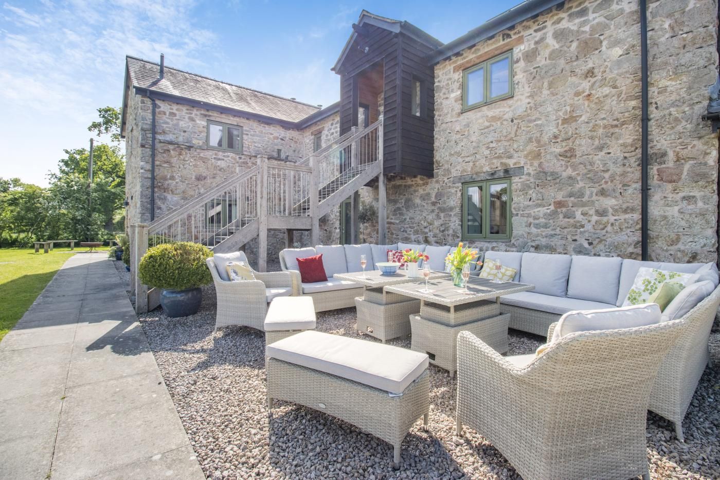A stone building with a staircase, outdoor seating area with wicker furniture, and a garden path.
