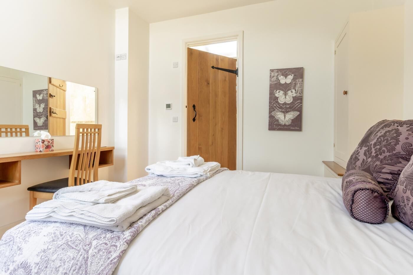 A bedroom with a bed, a wooden door, a chair, a desk, and a mirror.