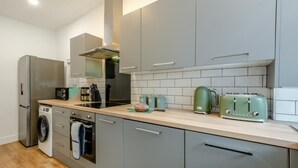 Ett kompakt kök med grå skåp, en inbyggd ugn, en mikrovågsugn, en brödrost och en vattenkokare.