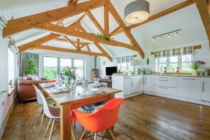 A spacious kitchen with wooden beams, a dining area with a table set for four, and a cozy living area with a sofa and a TV. - 3 Bed in Marhamchurch (oc-h29904) (Marhamchurch)