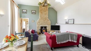 Un salón con chimenea de piedra, un televisor y un comedor con una mesa dispuesta para dos.