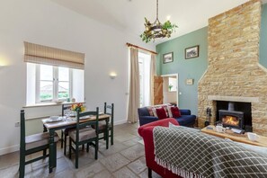 Ein gemütliches Wohnzimmer mit Kamin aus Stein, einem Essbereich mit Tisch und Stühlen sowie einem blauen Sofa.