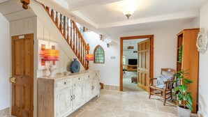 A spacious hallway with a wooden staircase, a white cabinet with decorative carvings, a wooden chair, and a potted plant. - 5 Bed in Hayle (oc-r42756) (Saint Erth Praze)