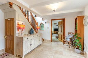 Ein geräumiger Flur mit einer Holztreppe, einem weißen Schrank mit dekorativen Schnitzereien, einem Holzstuhl und einem Blumentopf.