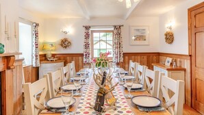 A dining room with a long table set for six, wooden paneling on the walls, a chandelier, and a window with curtains. - 5 Bed in Hayle (oc-r42756) (Saint Erth Praze)