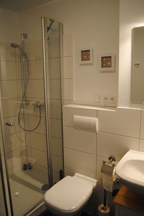 Ein Badezimmer mit einer Duschkabine, einer Toilette, einem Waschbecken und einem Spiegel.