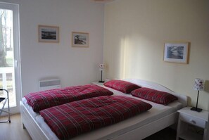 Ein Doppelbett mit roter Karo-Bettwäsche, ein Nachttisch, ein Sessel und gerahmte Bilder an der Wand.