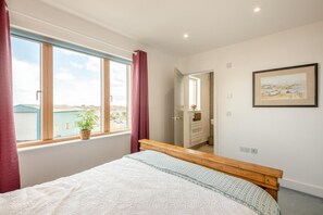 A bedroom with a bed, a window with curtains, a potted plant, a painting on the wall, and a view of buildings outside. - 3 Bed in Amble (oc-s43277) (Amble)