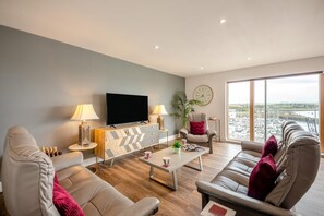 A modern living room with a flat-screen TV, two sofas, a coffee table, and a large window with a view of boats. - 3 Bed in Amble (oc-s43277) (Amble)