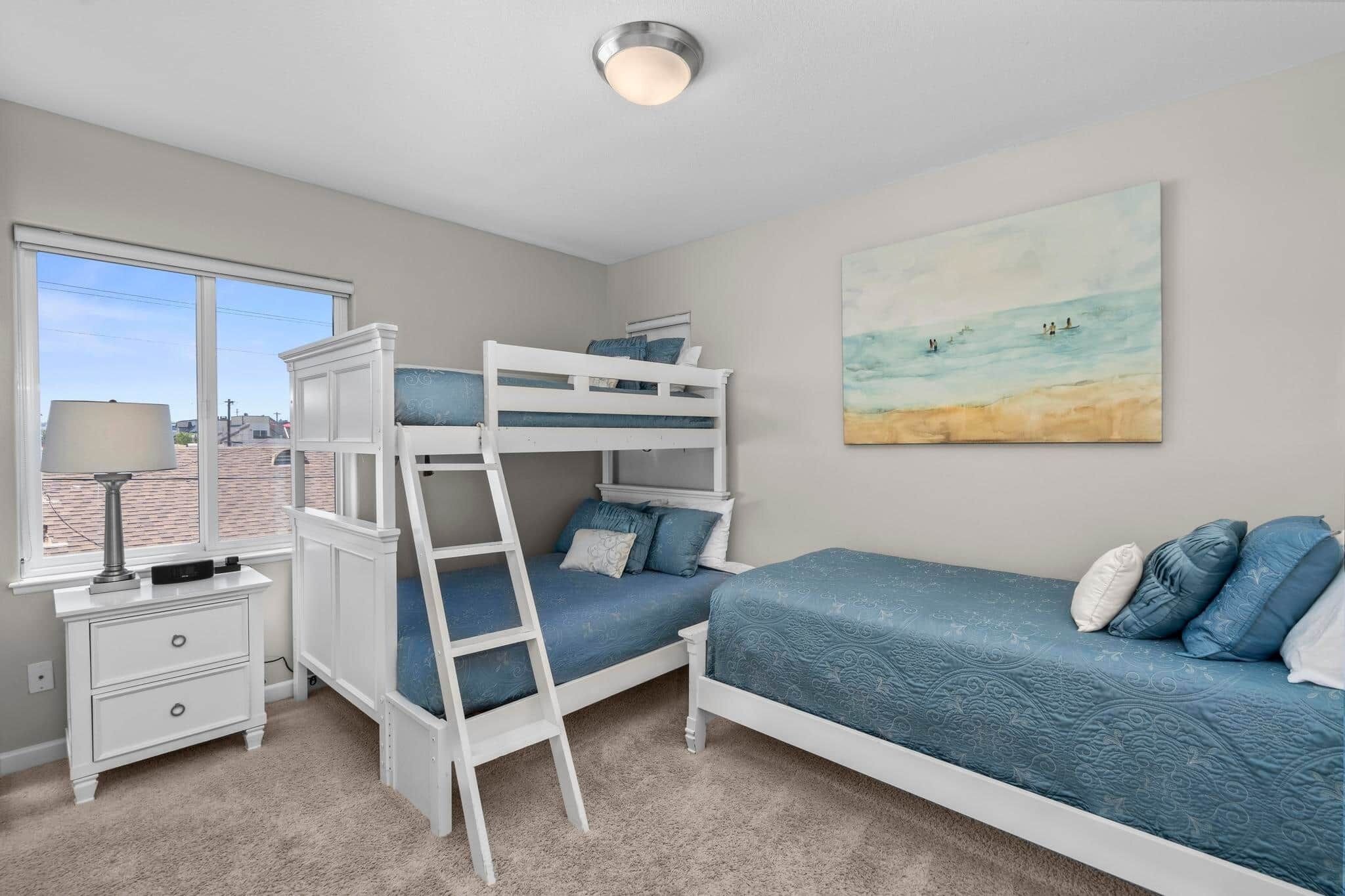 A bunk bed room with a desk, a lamp, and a beach-themed painting.
