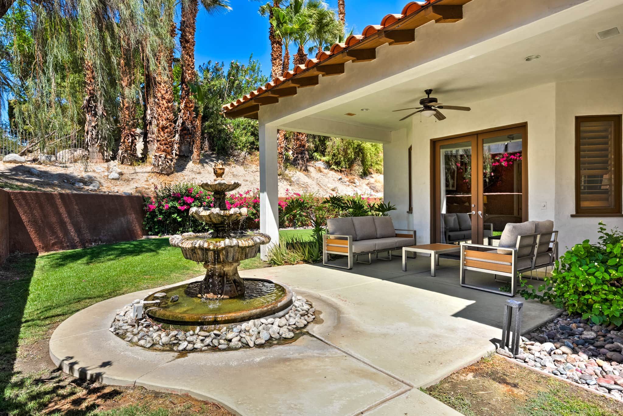 Un patio con mobiliario exterior, una fuente de piedra y vistas a un paisaje montañoso.