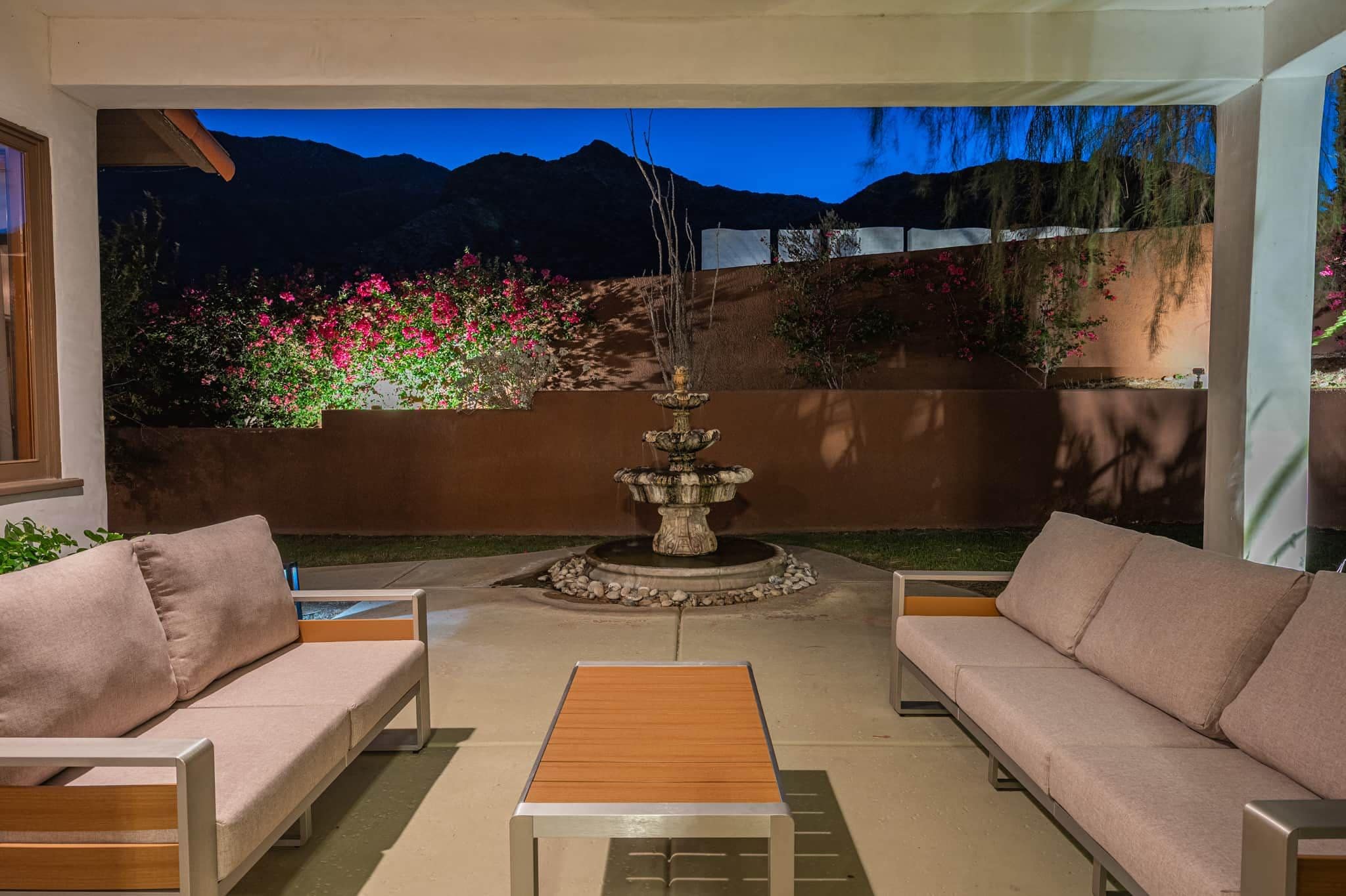 An outdoor patio with two sofas, a wooden coffee table, and a decorative fountain.