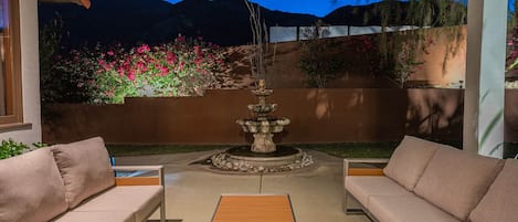 An outdoor patio with two sofas, a wooden coffee table, and a decorative fountain.