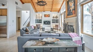 Un ampio soggiorno con soffitto in legno, un divano componibile grigio, un tavolino da caffè e una grande finestra con vista.