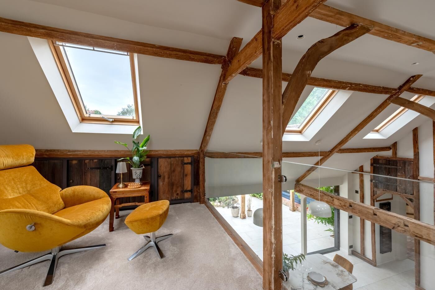 Une pièce de style « loft », avec des poutres en bois apparentes, une grande fenêtre, une chaise jaune, une petite table et une plante en pot.