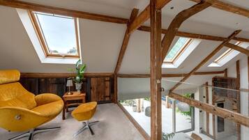 Une pièce de style « loft », avec des poutres en bois apparentes, une grande fenêtre, une chaise jaune, une petite table et une plante en pot.
