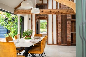 A dining area with a wooden ceiling, a table set for two, and a view of a brick wall and greenery outside.