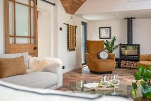 A cozy living room with a sofa, armchair, and a glass coffee table with wine glasses.