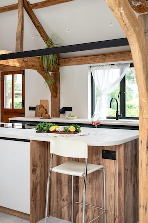 A kitchen with a wooden island, a white chair, and a window with a view of greenery.