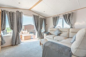 A spacious living area with a sofa and a small table, large windows with curtains, and a view of the outside. - 2 Bed in Cockermouth (oc-c43275) (Cockermouth)