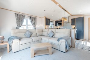 A modern living room with a sectional sofa, a wooden coffee table, and a kitchen in the background. - 2 Bed in Cockermouth (oc-c43275) (Cockermouth)
