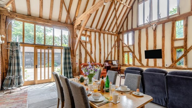 A rustic interior with exposed wooden beams, a dining area with a table set for breakfast, and a seating area with cushions. - 3 Bed in Chediston (oc-b43313) (Chediston)