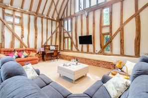 Ein Zimmer mit freiliegenden Holzbalken, einem Klavier, einem Fernseher und einem großen Fenster.