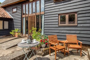 A wooden house with a patio, two wooden chairs, a table, and potted plants. - 3 Bed in Chediston (oc-b43313) (Chediston)